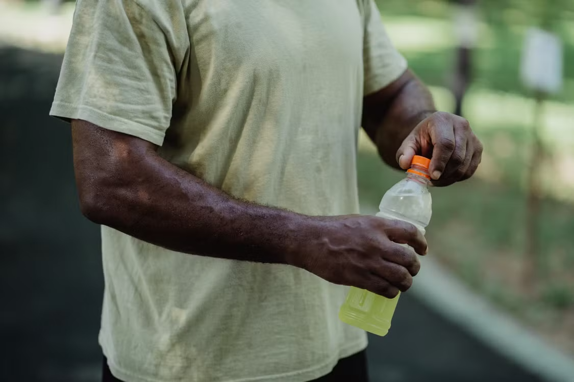 Consumer opening a bottled yellow hydration drink outdoors