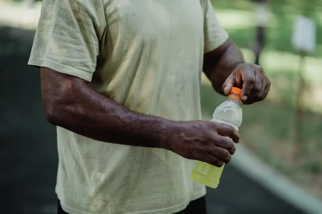 Consumer opening a bottled yellow hydration drink outdoors